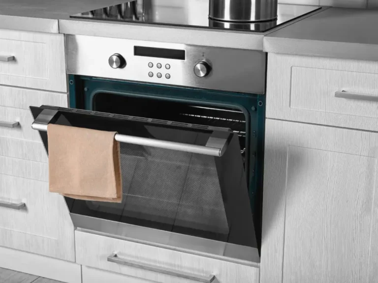 Four encastré ouvert avec torchon suspendu sur la porte, dans une cuisine aux façades claires - réparation four Genève, Suisse Dépannage