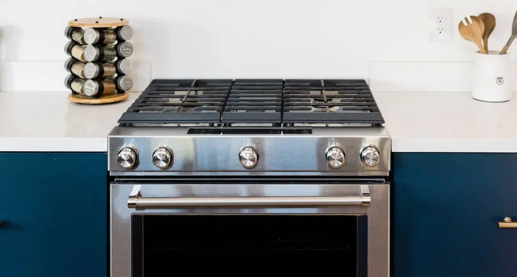 Cuisinière inox avec plaque de cuisson à gaz et four intégré dans une cuisine bleu marine - réparation cuisinière Genève, Suisse Dépannage