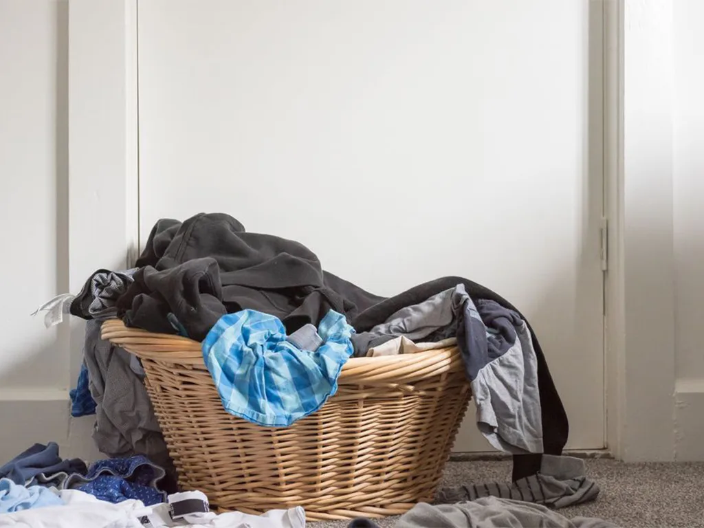 Panier en osier débordant de linge sale entassé dans une entrée - réparation lave-linge Genève, Suisse Dépannage
