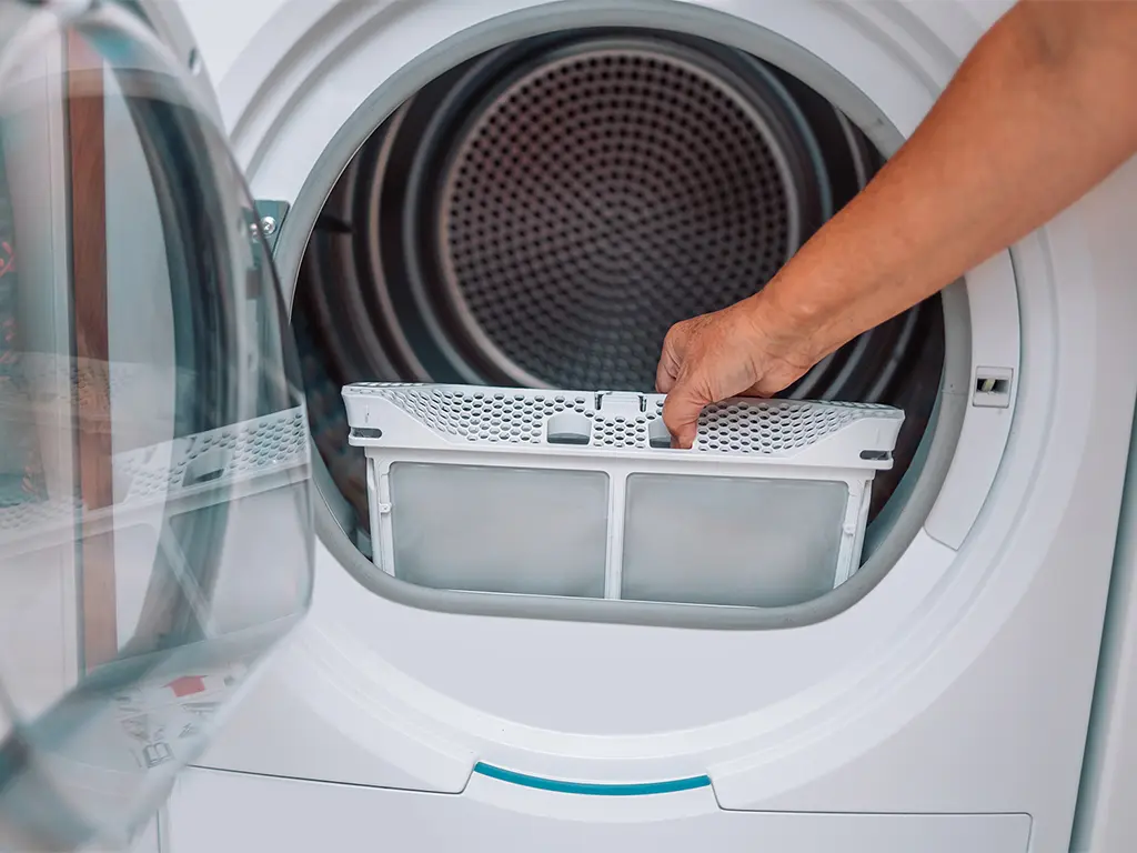 Main retirant le filtre à peluches d'un sèche-linge - entretien et réparation sèche-linge Genève, Suisse Dépannage